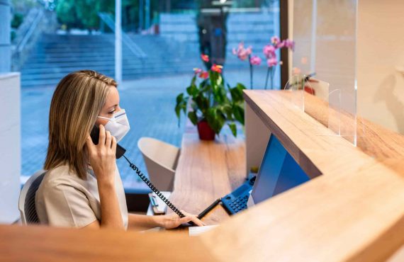young woman answer the phone at the reception with coronavirus mask