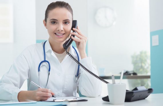 Young female doctor answering expert sitting at her desk and talking on the phone