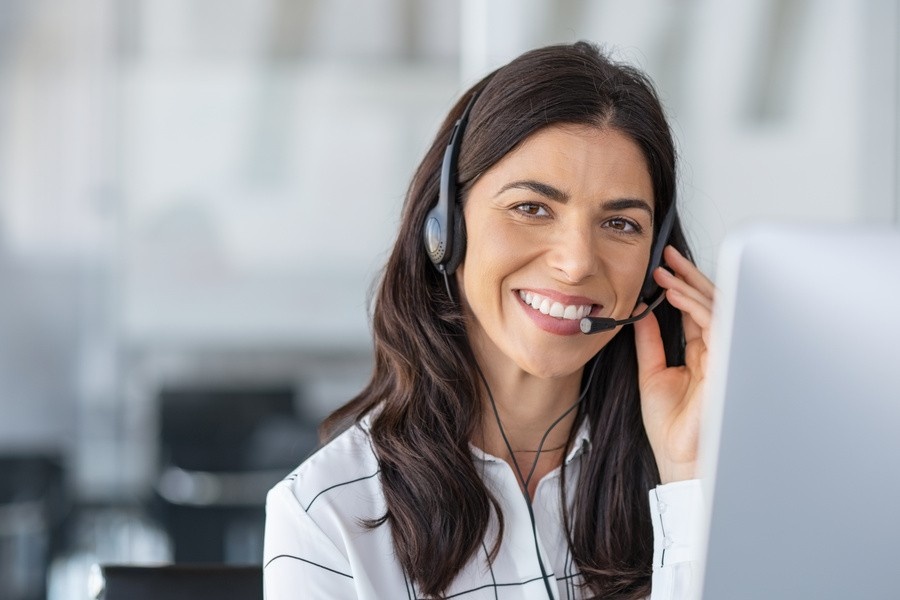 Call center agent with headset working on support hotline in modern office with copy space. Portrait of mature positive agent in conversation with customer over headset looking at camera. Consulting and assistance service in medical setup